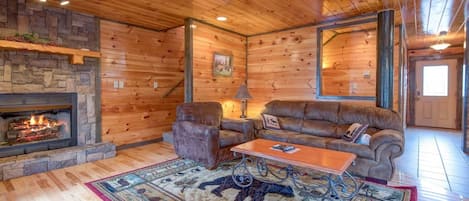 A log cabin interior with a stone fireplace, leather furniture, and a large mirror.