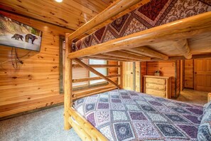 L’intérieur d’une cabane en bois, avec un lit superposé, un petit bureau et un tableau représentant un ours accroché au mur.