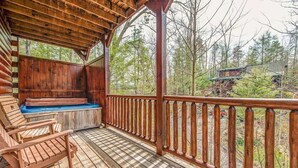 Een houten terras met een jacuzzi en zitgedeelte, omgeven door een houten balustrade en bomen.