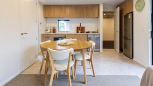 A modern kitchen with wooden cabinets, a dining table with chairs, and a refrigerator. - Central City House with Garage | Walk to Stadium (Christchurch)