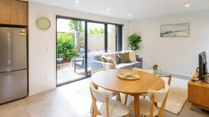 A modern kitchen with a dining area, a refrigerator, and a large sliding glass door leading to a patio with outdoor furniture. - Central City House with Garage | Walk to Stadium (Christchurch)