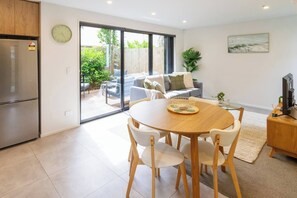 A modern kitchen with a dining area, a refrigerator, and a large sliding glass door leading to a patio with outdoor furniture. - Central City House with Garage | Walk to Stadium (Christchurch)
