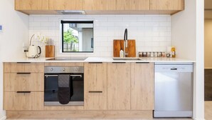 A modern kitchen with wooden cabinets, a built-in oven, a dishwasher, and a large window above the sink. - Central City House with Garage | Walk to Stadium (Christchurch)
