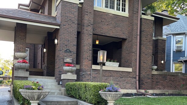 Una casa de dos pisos con fachada de ladrillo, un porche cubierto y una entrada principal con escalones que llevan a la puerta.