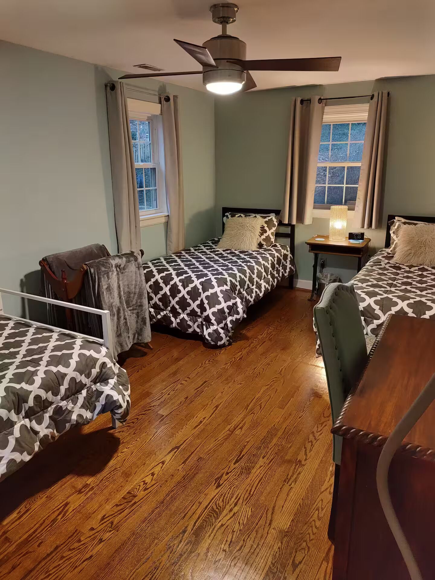 A room with two beds, a ceiling fan, and a nightstand with a lamp.