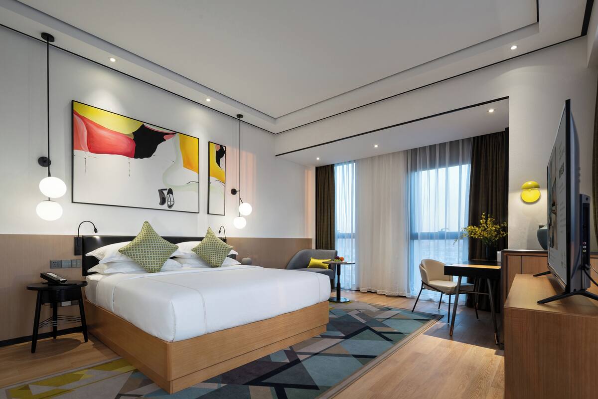 A modern hotel room with a large bed, a desk, a chair, and a television.
