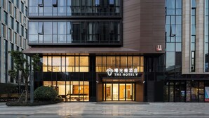 A modern hotel with a glass facade, a prominent sign reading "The Hotel V," and a well-maintained outdoor area with a small tree and a bench. - The Hotel V Hongqiao  (Shanghai)