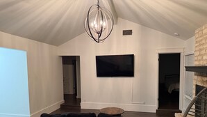 A modern living room with a black sectional sofa, a round coffee table, a large flat-screen TV mounted on the wall, and a unique chandelier.