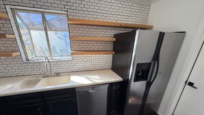 A kitchen with a stainless steel refrigerator, a dishwasher, a sink, and a window above the sink.