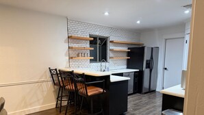 A compact kitchen with a white tiled backsplash, a black refrigerator, a dishwasher, and a wooden bar counter with stools.