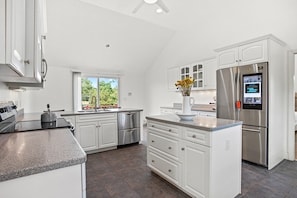 A modern kitchen with white cabinetry, stainless steel appliances, a granite countertop, and a window with a view of greenery. - Elegant + relaxing + water views + Cape Cod experience (Bourne)