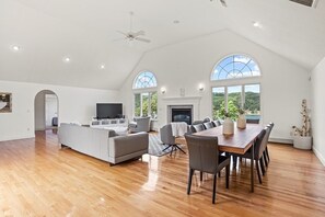 A spacious living area with a fireplace, a dining table, and a TV. - Elegant + relaxing + water views + Cape Cod experience (Bourne)