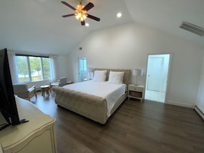 A spacious bedroom with a large bed, a ceiling fan, and a view of the outdoors through a window. - Elegant + relaxing + water views + Cape Cod experience (Bourne)