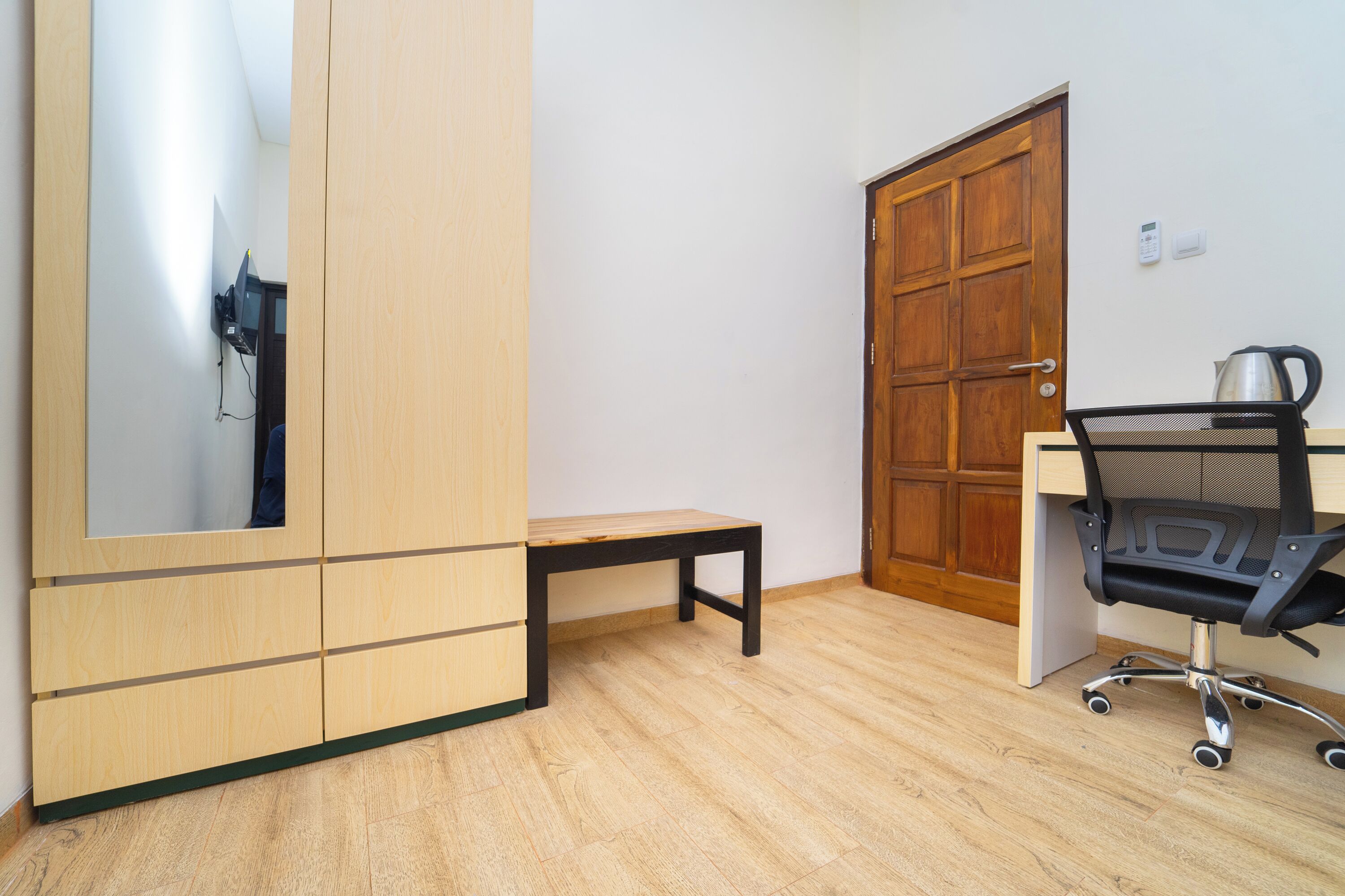 Una habitación con un armario de madera, un pequeño banco de madera, un escritorio con silla y una puerta de madera.