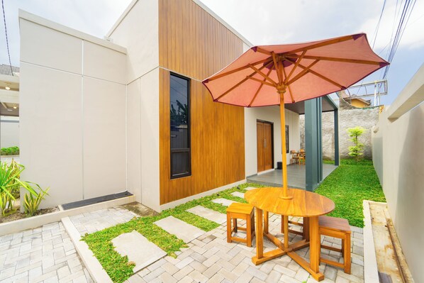 A modern patio with a wooden table and chairs, a red umbrella, and a small garden area with stepping stones. - Semenrante Living by ARBA (Surakarta)