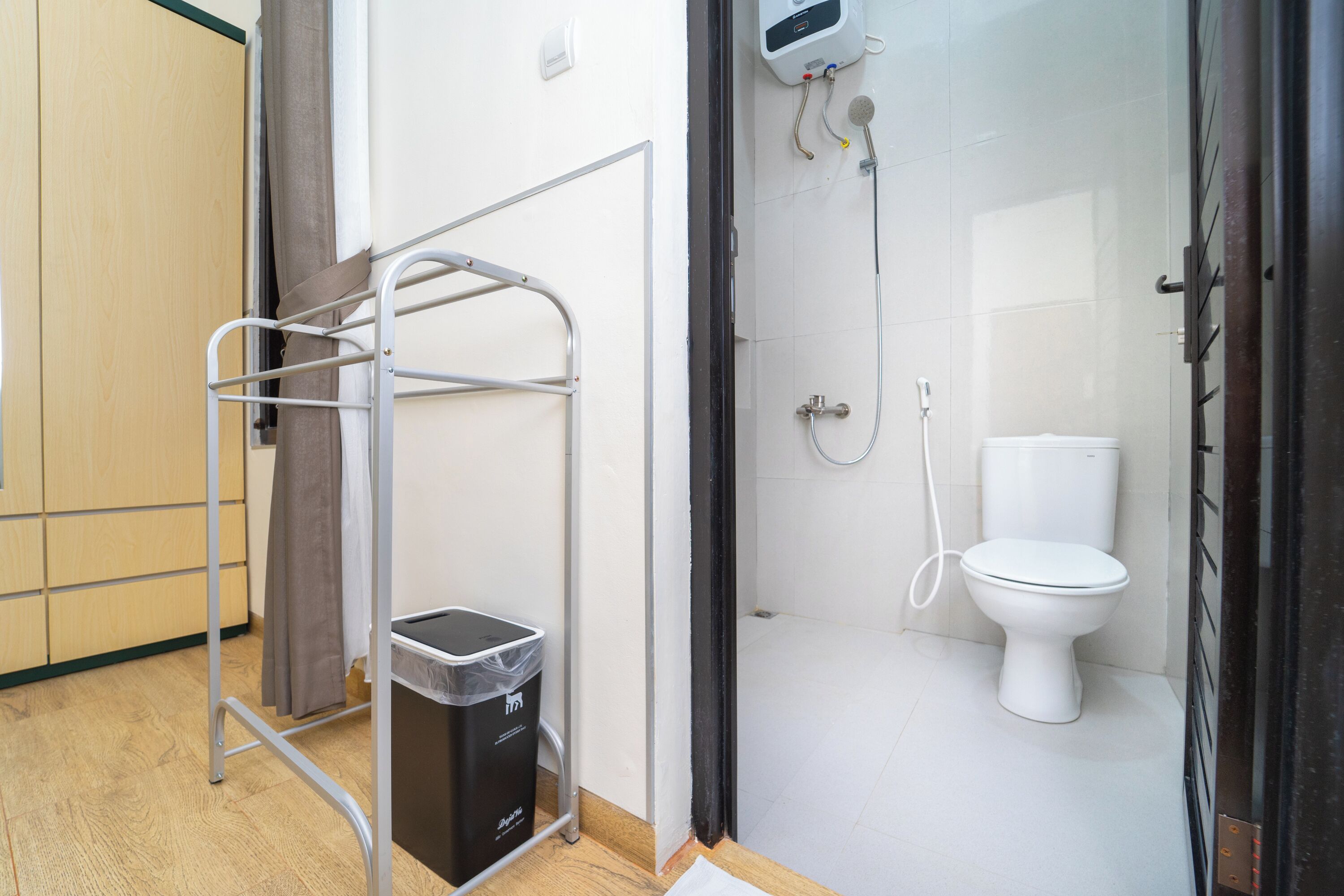 Un baño con ducha, inodoro y un tendedero metálico con un cubo de basura.