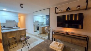 Una cucina moderna con isola centrale, un'area pranzo con sgabelli, una TV a parete e un piccolo tavolo con un asciugamano.