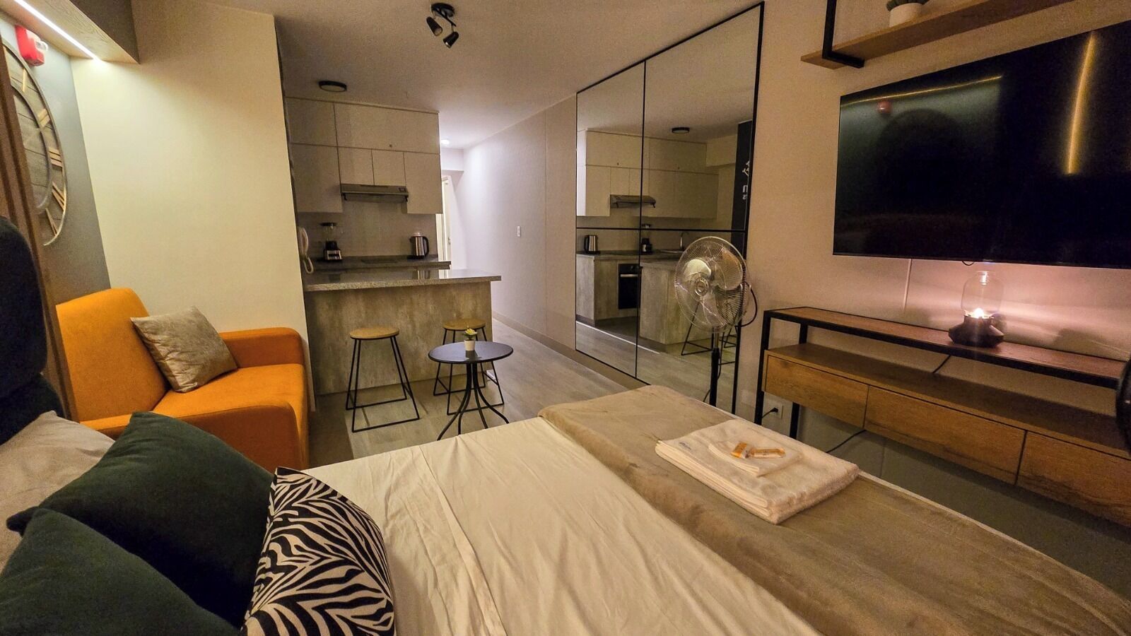 Een moderne hotelkamer met een bed, een bank, een kitchenette en een televisie.