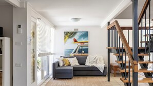 Ein Wohnzimmer mit grauem Sofa, einem Surfbrett-Gemälde und einer Treppe.