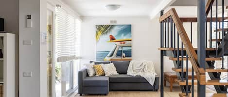 Uma sala de estar com um sofá cinzento, um quadro de um prancha de surf e uma escadaria.