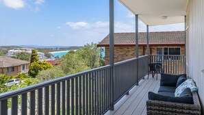 Ein Balkon mit Blick auf Strand und Häuser, eine Korbsitzgruppe und ein Tisch mit Stühlen.