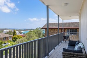 Ein Balkon mit Blick auf Strand und Häuser, eine Korbsitzgruppe und ein Tisch mit Stühlen.