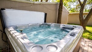 Un jacuzzi con tapa, rodeado por una terraza de madera y una valla.