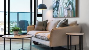 Un salon moderne avec un canapé, deux tables d’appoint, une plante en pot et un grand tableau abstrait.