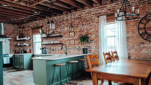 A kitchen with a brick wall, wooden ceiling beams, a large island with stools, and a dining table with chairs. - Twin Bricks Railhouse near Route 66 (Bourbon)