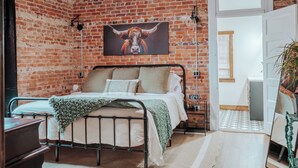 A bedroom with a brick wall, a bed with a metal frame, a nightstand, and a mirror. - Twin Bricks Railhouse near Route 66 (Bourbon)