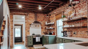 A kitchen with a brick wall, wooden beams, and green cabinets. - Twin Bricks Railhouse near Route 66 (Bourbon)