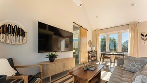 A modern living room with a flat-screen TV, a sofa, a coffee table, and a dining area with a table and chairs. - NEW: Sol + Shadow | Pool | Spa | Walk to Downtown (Joshua Tree)