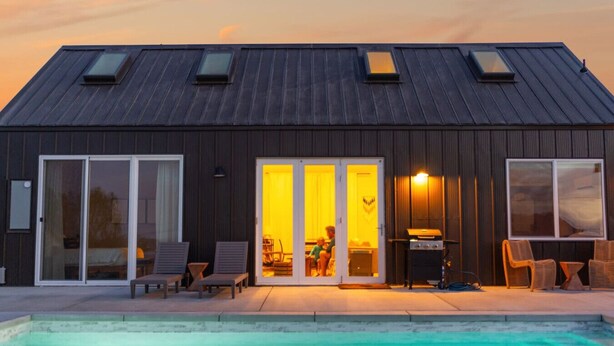 A modern house with a swimming pool, large sliding glass doors, and a patio with outdoor furniture. - NEW: Sol + Shadow | Pool | Spa | Walk to Downtown (Joshua Tree)