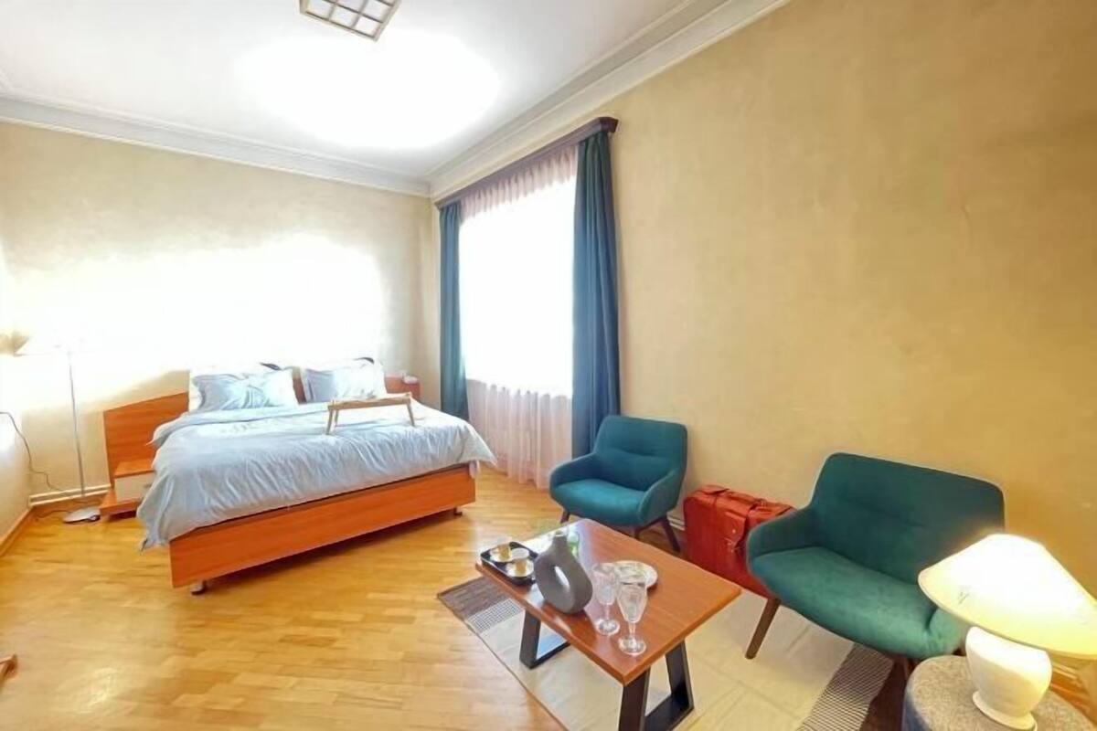 A hotel room with a bed, a desk, two chairs, a lamp, and a window with curtains.