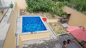 Een zwembad op het dak met een betegeld zonnedek en een kleine tuin met planten en bloemen.