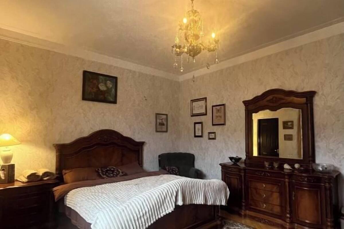 A bedroom with a wooden bed, a dresser, a mirror, and a chandelier.