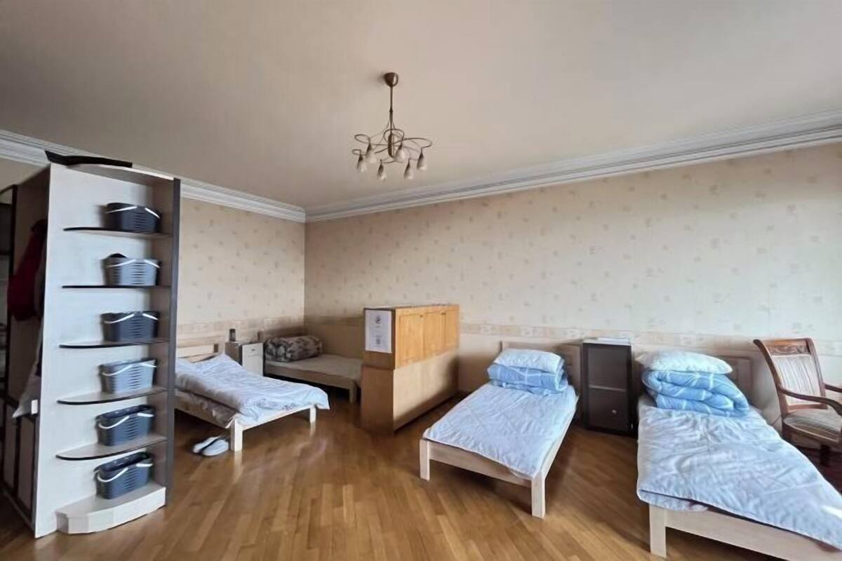 A room with two beds, a desk, a wardrobe, and a hanging light fixture.