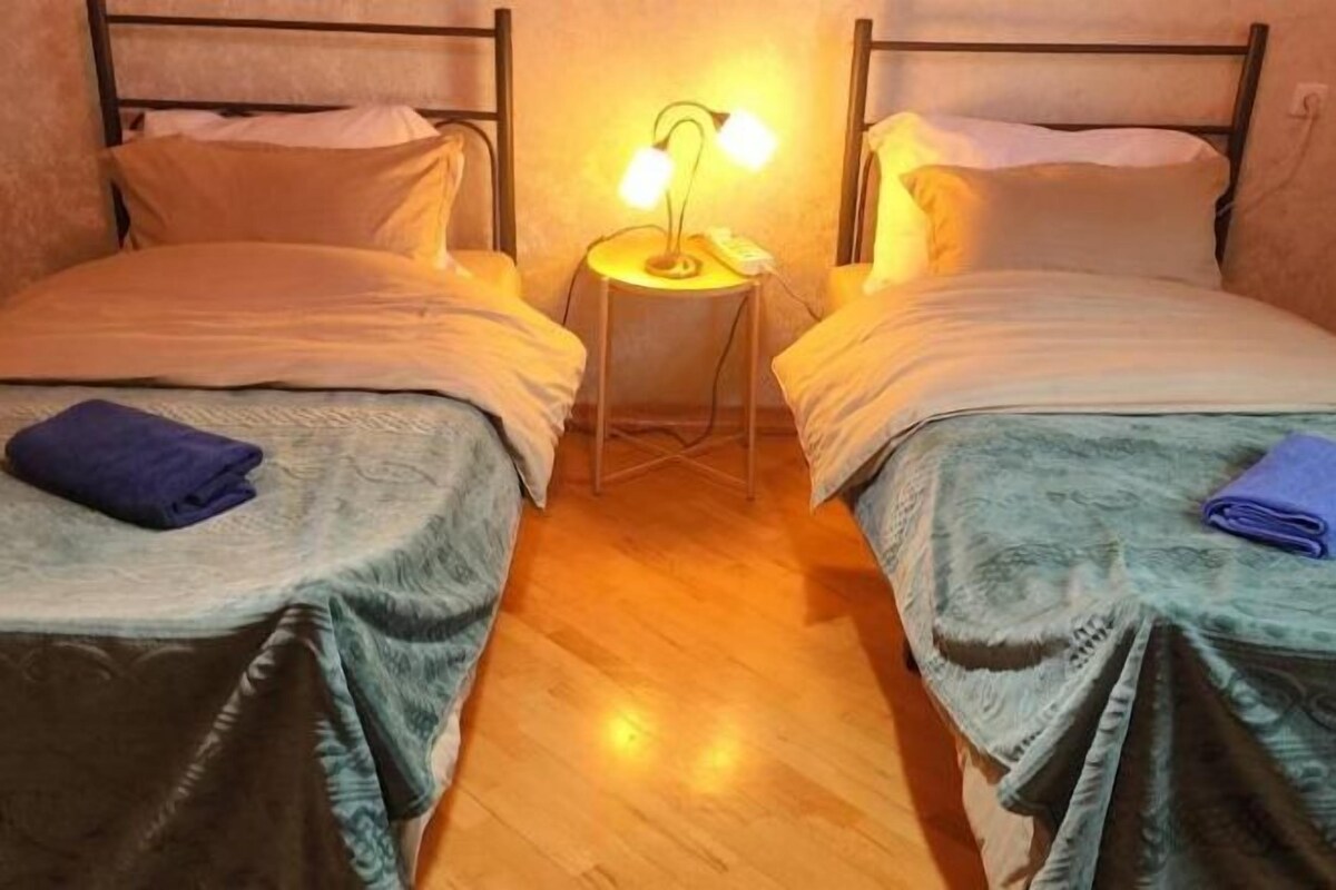 A twin room with two beds, a nightstand with a lamp, and a wooden floor.