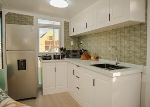 A modern kitchen with white cabinets, a stainless steel refrigerator, a built-in oven, a sink, and a window providing a view of the outside. - Cozy 2BR Villa• Private Pool and Patio• Hot water• Aruba Tropical Getaway (Oranjestad)