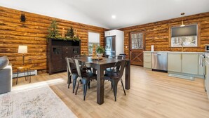 Een moderne keuken met houten wanden, een eetgedeelte met een houten tafel en stoelen, en uitzicht op de omgeving door een raam.