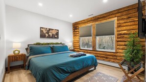 Een moderne slaapkamer met een groot bed, houten lambrisering, een wereldkaart schilderij en een raam met uitzicht op bomen.