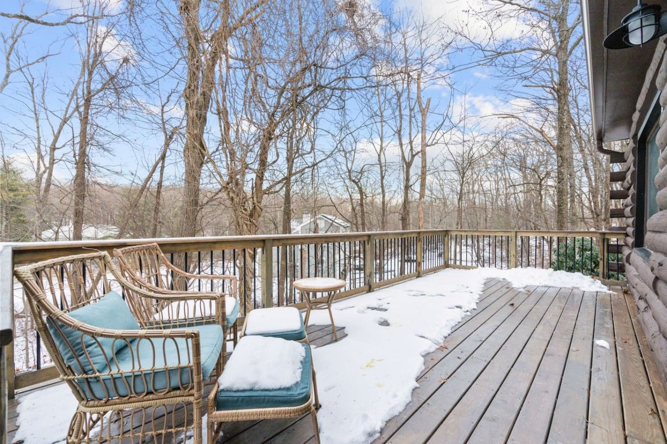Une terrasse en bois, meublée de meubles en osier et dotée d’une rambarde, entourée d’arbres et de neige.