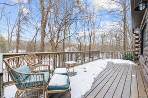 A wooden deck with wicker furniture and a railing, surrounded by trees and snow.