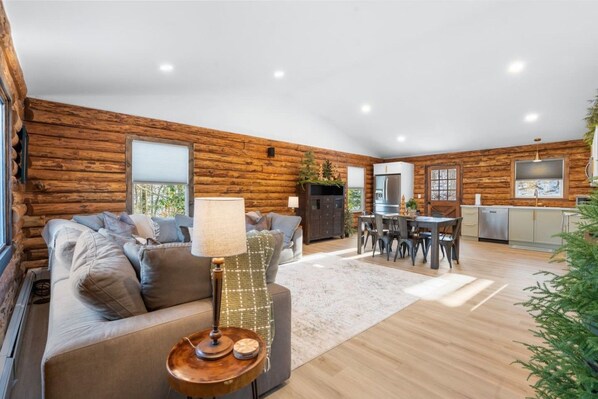 A log cabin interior with a living room, dining area, and kitchen.