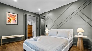 Un dormitorio moderno con una cama, dos mesitas de noche, un banco y una obra de arte colgada en la pared.