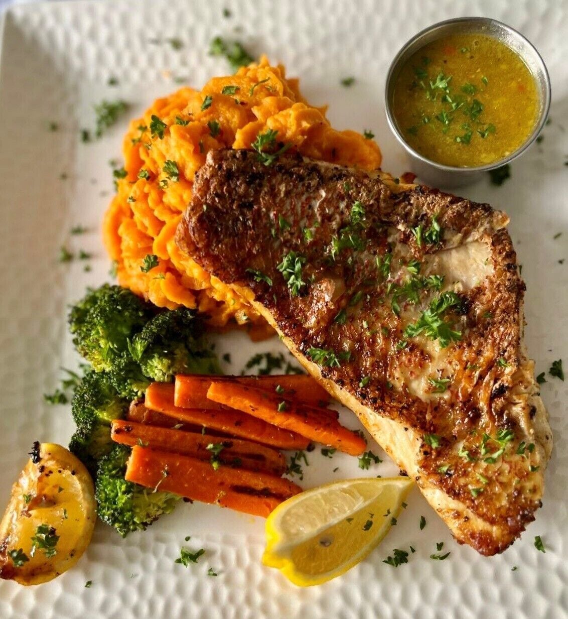 A plate with a grilled fish fillet, roasted vegetables, and a side of mashed sweet potatoes.