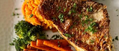 A plate with a grilled fish fillet, roasted vegetables, and a side of mashed sweet potatoes.