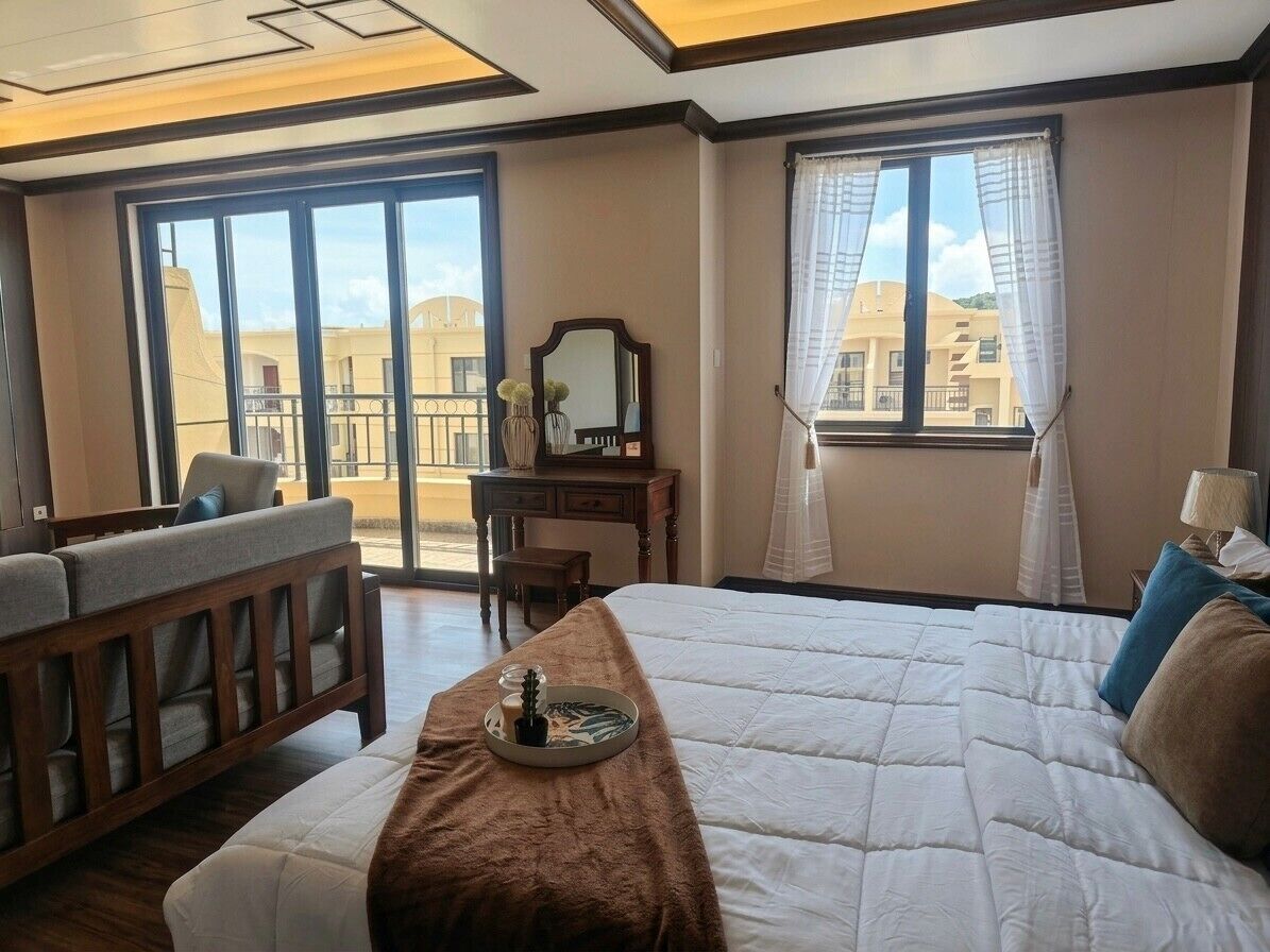 Ett hotellrum med en stor säng, en soffa, ett skrivbord och utsikt över byggnader genom fönstren.