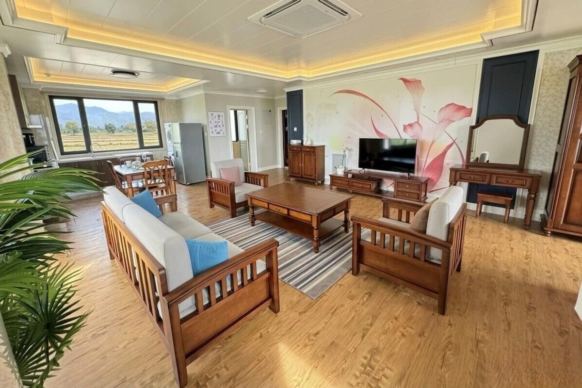 Ein geräumiges Wohnzimmer mit Holzmöbeln, einem großen Fernseher und Blick ins Freie.