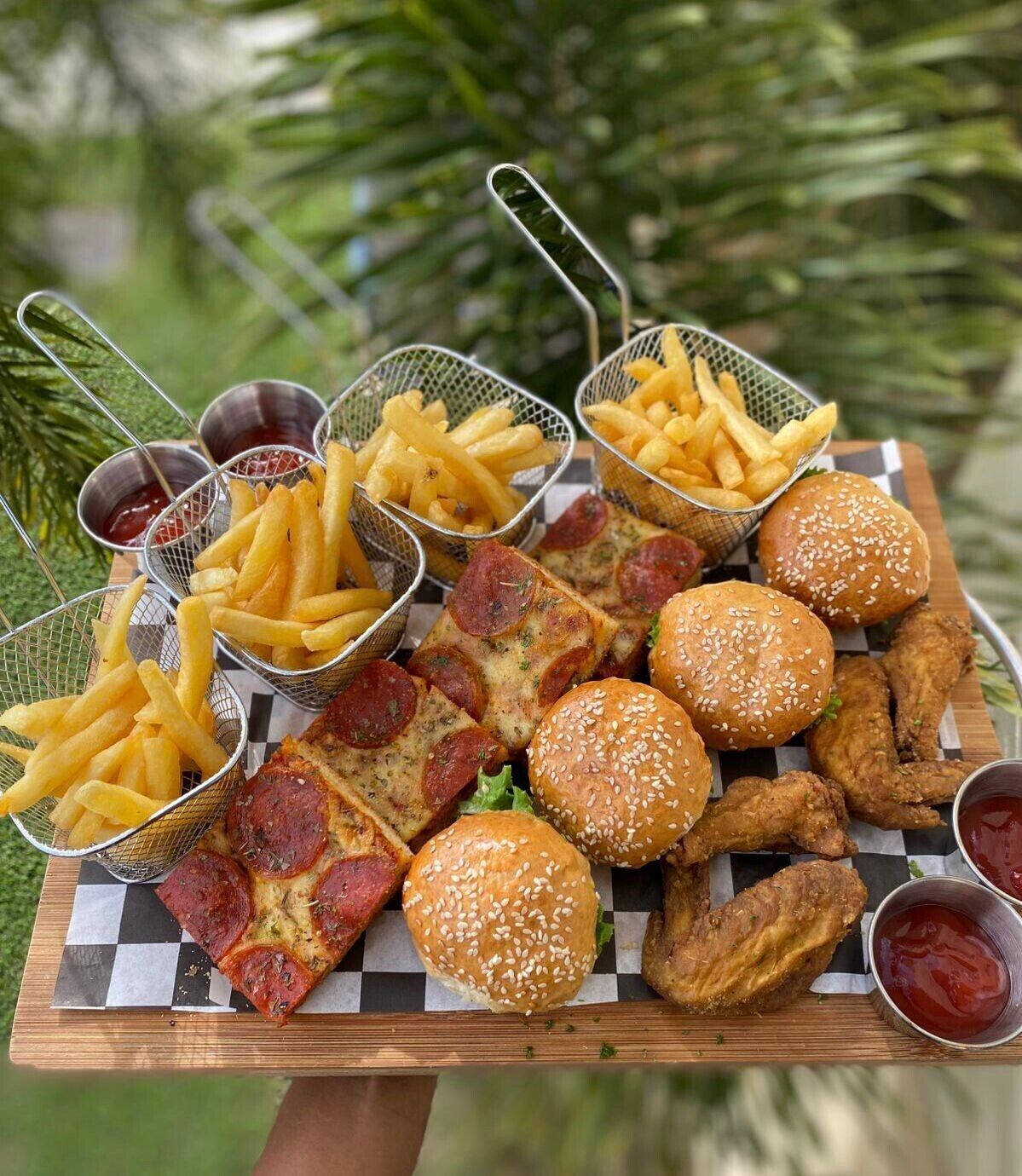Une table en bois sur laquelle on trouve une variété de plats frits, notamment des hamburgers, des ailes de poulet et des frites, accompagnés de ketchup.